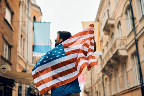 Preview: Back view of sports fan covered with American national flag walking on the street.