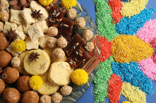 Preview: Diwali celebration. Tasty Indian sweets, spices, nuts and colorful rangoli on blue table, flat lay