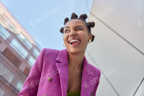 Preview: Underside view of cheerful stylish woman winks eye sticks out tongue has fun while walking in urban