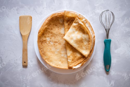 Preview: Round thin pancakes lie on a plate. Nearby lies a whisk and a spatula for cooking.