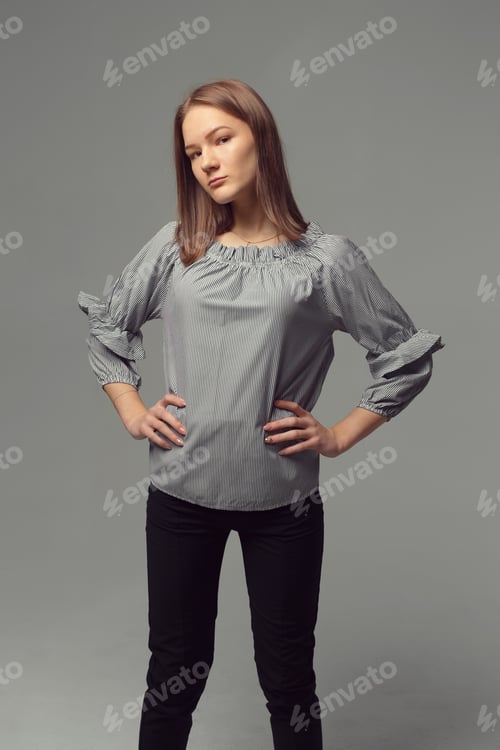 Preview: Young woman posing confidently in a studio with gray background and stylish top