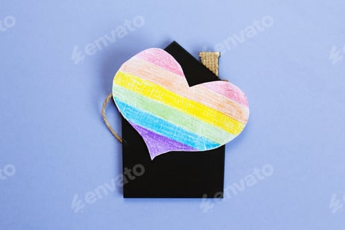 Preview: heart in the form of a lgbt flag next to a miniature toy house