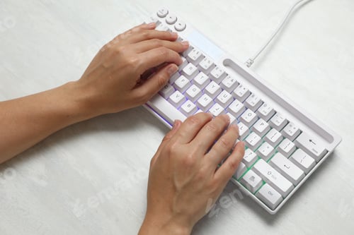 Preview: Woman typing on modern keyboard with RGB lighting at white wooden table, above view
