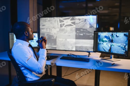 Preview: African American security officer or dispatch uses computer and walkie talkie, looks at screens