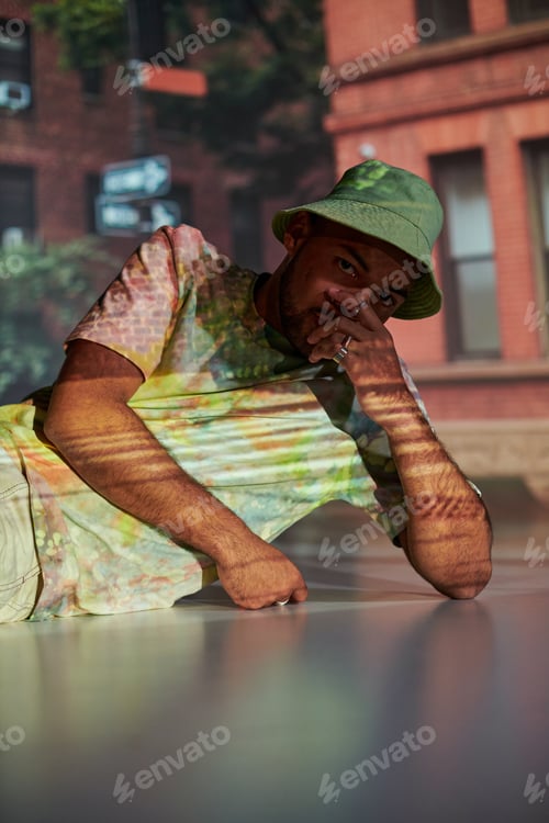 Preview: good looking man half lying on floor in stylish outfit in digital projector lights, fashion concept