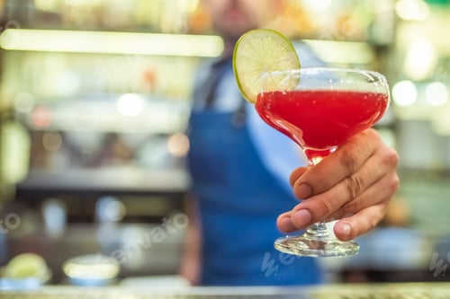 Preview: The barman holding a red cocktail with a citrus