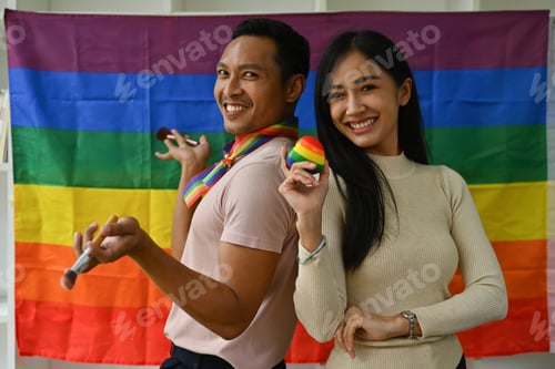 Preview: Confident gay male and friend standing against LGBTQ rainbow flag and smiling to camera