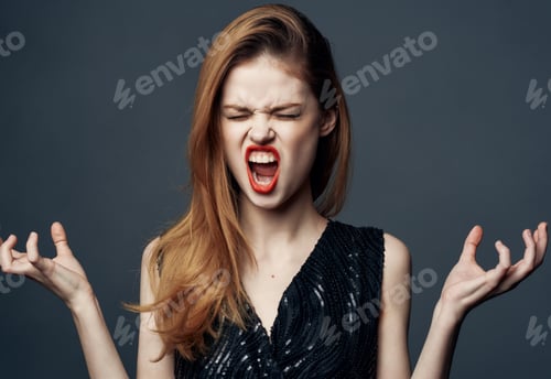 Preview: Portrait of emotional woman in a black dress on a gray background with bright makeup and shadows on