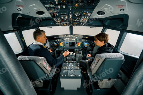 Preview: An experienced pilot instructs a young student before a training flight in the cockpit simulator