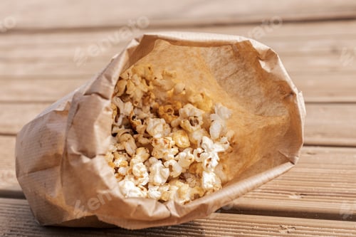 Preview: A brown paper bag is tipped over, spilling fluffy popcorn onto a weathered wooden surface.
