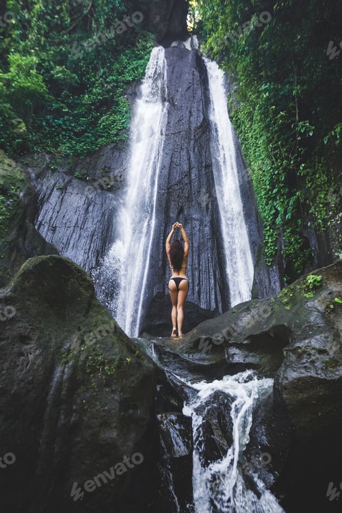 Preview: Woman enjoying near hidden in jungle cascade waterfall in Bali. Slim body and black swimsuit