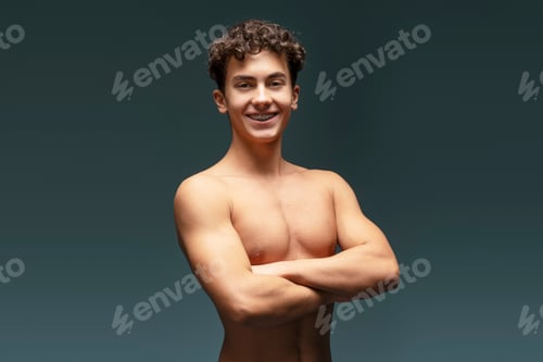 Preview: Portrait of attractive teen boy with bare torso, crossed arms posing isolated on gray background