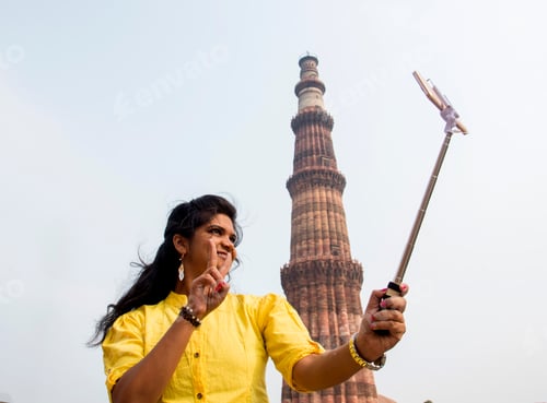 Preview: Tourist woman taking selfie in front of Qutub Minar, Delhi, India.