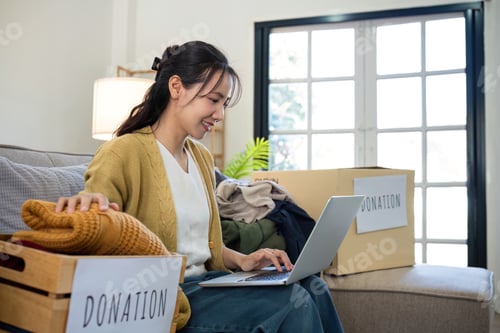 Preview: Asian woman uses laptop to search for clothing donation options to pass on unused clothing to others