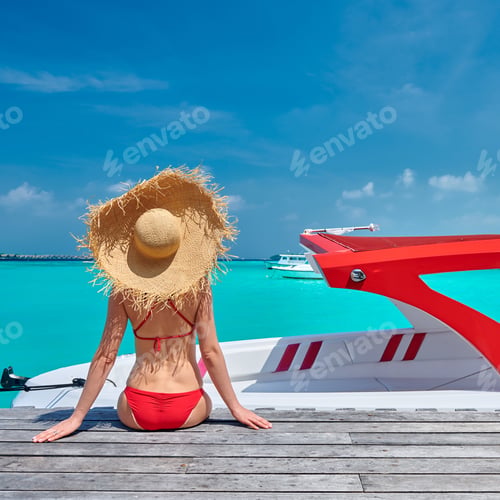 Preview: Woman in bikini sitting on jetty with boat