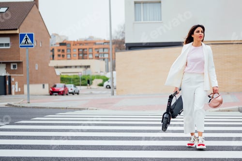 Preview: Smiling young man crossing the street with an electric scooter in his hand walking through the city
