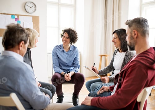 Preview: Men and women sitting in a circle during group therapy, talking.