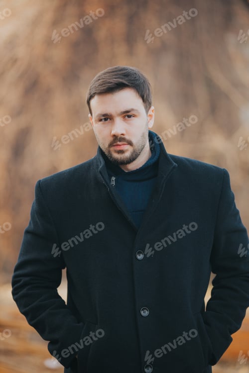 Preview: Vertical shot of a handsome Caucasian male with a black coat posing outdoors