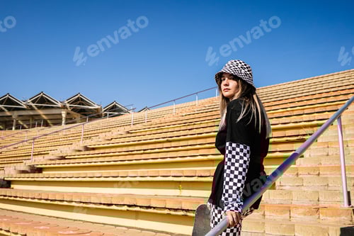 Preview: Stylish woman with skateboard leaning on railing
