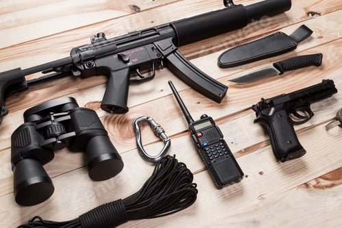 Preview: Assault rifle, gun, knife with sheath, compass and notebook with pen on table.