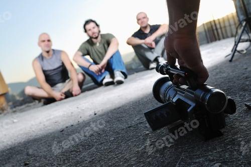 Preview: Three Young Man Siting On Ground While Modern Video Camera Recording