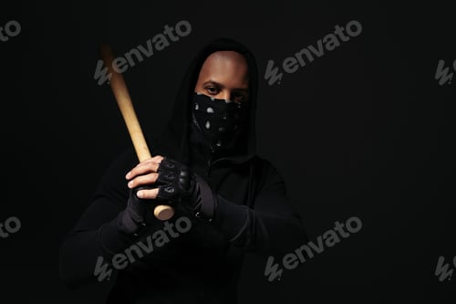 Preview: African american hooligan in mask on face and glove holding baseball bat isolated on black