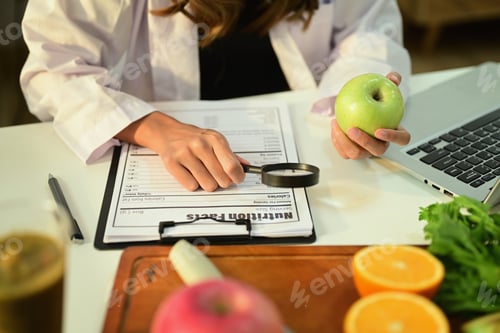 Preview: Cropped image of nutritionist holding an apple and prescribing recipe at desk with fresh fruit.