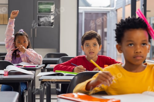 Preview: Biracial girl raises her hand in a school classroom; biracial boy in red looks curious
