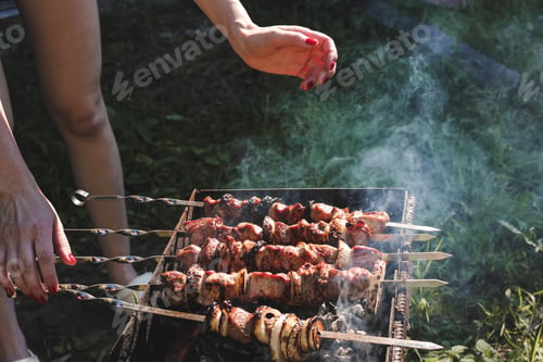 Preview: Juicy meat on barbecue skewers cooking by young woman in backyard in summer. Food background. BBQ