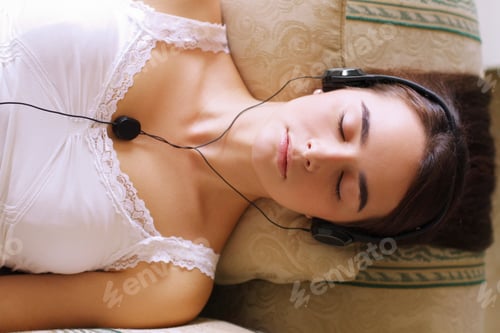 Preview: An attractive young woman listening to music while dozing on the sofa
