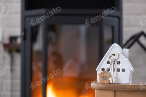 Preview: Key to house with keychain against background of fireplace stove with fire and firewood