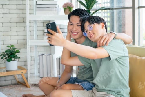 Preview: Couple gay or lgbt man enjoy with mobile phone together and sitting on sofa near bed