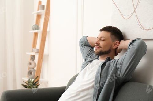 Preview: Handsome man relaxing on sofa at home, space for text