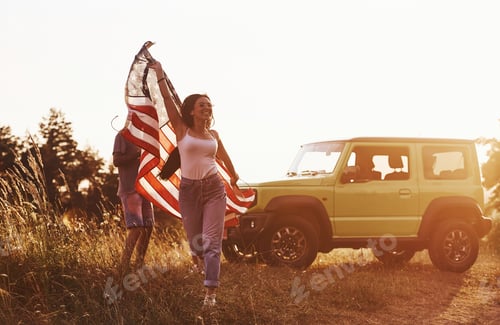 Preview: Girl runs forward. Friends have nice weekend outdoors near theirs green car with USA flag