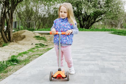 Preview: Little toddler girl learns to ride kick scooter in city park on spring day.