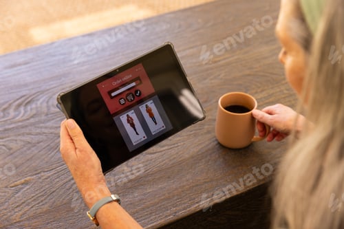 Preview: Browsing clothing options on tablet, mature woman holding coffee cup at home