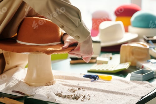 Preview: Close-up of young artisan fixing brim edges of felt panama hat to workpiece