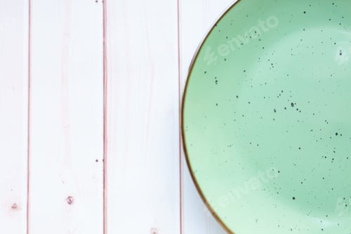 Preview: Light green ceramic plate with on white wooden background. Top view