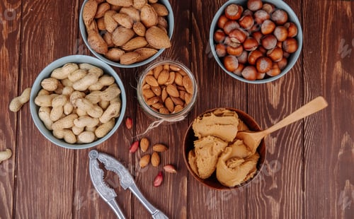 Preview: top view of mixed nuts and a bowl with peanut butter with a nut cracker on wooden background