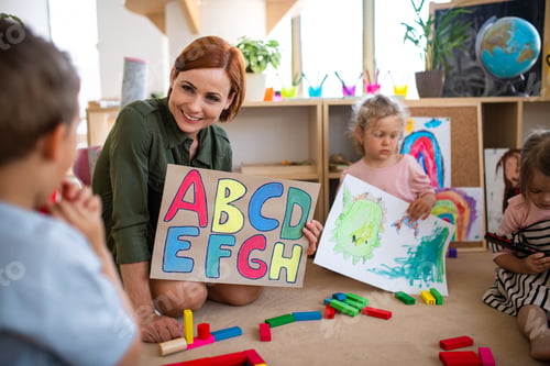 Preview: Group of small nursery school children with teacher on floor indoors in classroom, learning