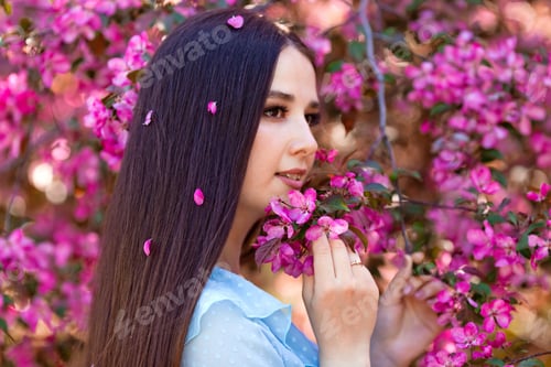 Preview: A brunette girl with long hair is standing near a pink blooming tree