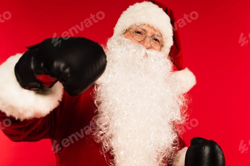 Preview: Santa claus in eyeglasses and boxing gloves looking at camera isolated on red