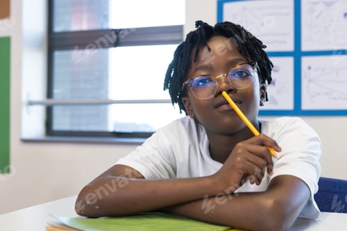 Preview: In school, african american boy playfully holding pencil under nose while sitting at desk