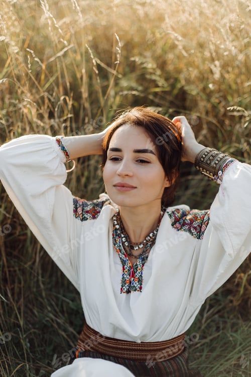 Preview: Young woman in traditional national embroidered shirt and skirt on nature at sunset.