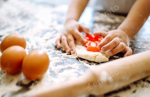 Preview: Close up of boy hands carving dough with cookie heart cutters. Easter baking preparation.