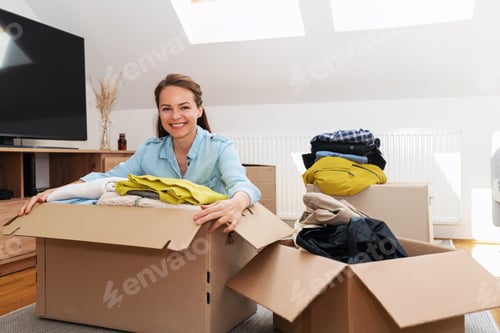 Preview: Young woman packing her own clothes to send to charitable organisation.