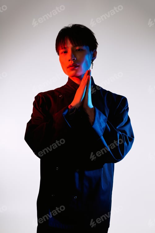 Preview: Stylish asian young man striking a pose with folded hands against vibrant backdrop