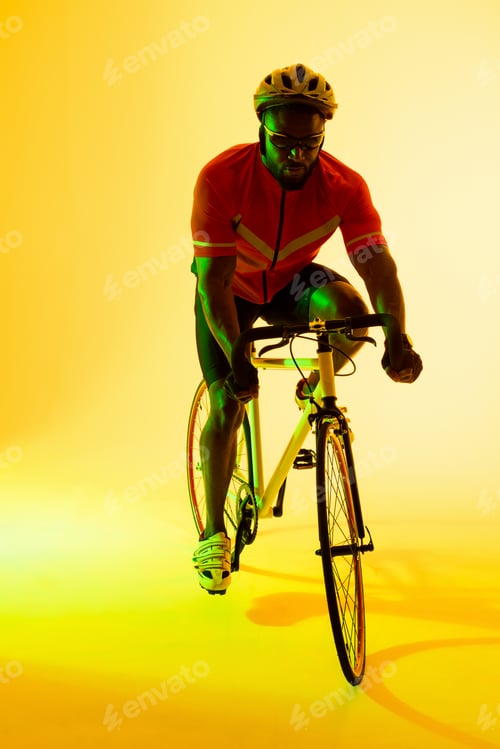 Preview: Vertical image of african american male cyclist riding bike in yellow lighting