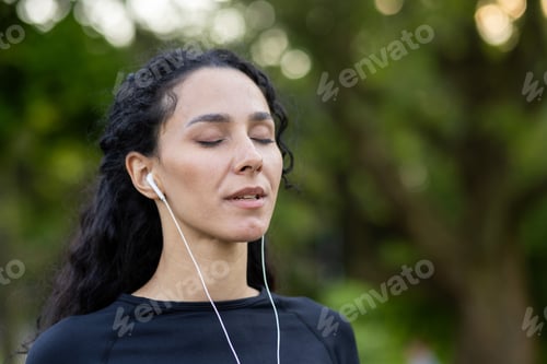 Preview: Portrait of a young woman in headphones with eyes closed, walking in the park in the morning