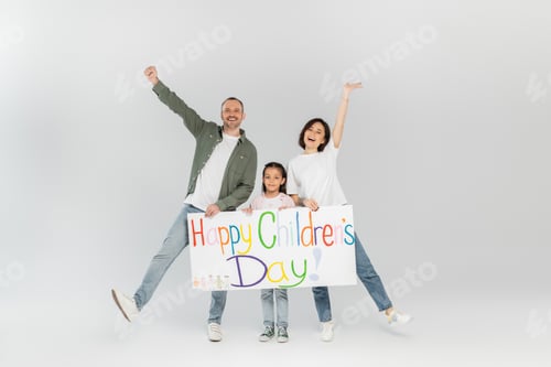 Preview: Full length of excited parents in casual clothes looking at camera while holding placard with happy